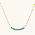 Gold-plated curved necklace and hoop earrings with turquoise cubic zirconia stones on white background.