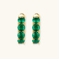 Close-up of gold-plated huggie hoop earrings featuring four emerald green cubic zirconia stones on white background.