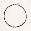Beaded black agate necklace with iridescent baroque freshwater pearl centerpiece on cream background.